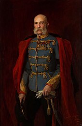 Peinture en pied d'un militaire, le crâne nu, les moustaches épaisses, portant une veste bleu avec des brandebourgs dorés et revêtu d'un lourd manteau dont on ne voit que les revers rouge vif.