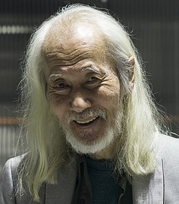 un vieil homme asiatique souriant, aux longs cheveux blancs et courte barbe blanche
