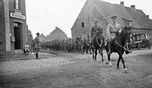 Photographie en noir et blanc d'un officier à cheval conduisant des troupes à pied.