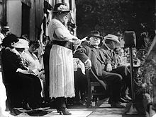 Photographie noir et blanc d'une femme debout prenant la parole lors d'un meeting