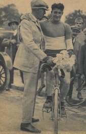 Photographie d'un cycliste sur son vélo, un bouquet à la main, un homme le soutenant.