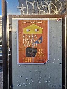 Cartaz colado em paragem de autocarro. O cartaz tem fundo cor de laranja e uma esquadria branca. O cartaz tem uma mão preta que agarra um caule que tem uma folha e uma casa, no lugar da flor. Tem letras a branco que indicam o mote da manifestação e o local da manifestação.