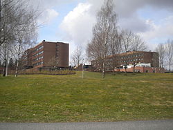 Two brown brick buildings about five floors tall and a lawn in the foreground.