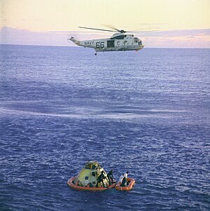 Photograph of a helicopter hovering above ocean with the Apollo 10 capsule and astronauts floating nearby