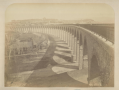 Photographie en sépia montrant le viaduc terminé, prise depuis la gauche de la balustrade de sécurité du pont qui fuit vers la gauche de l'image.