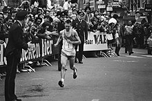 Photo of Cor Vriend running on the street with an audience behind fences