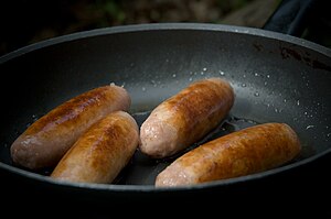 Sausages frying in pan on camping stove at Hol...