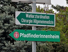 The lower sign PfadfinderInnenheim
points to a Scouting residence for Boy- and Girl Scouts.

The upper sign Wahlarztordination Chirurgie/Allgemeinmedizin
, roughly "Private Doctor Consultation Surgery/General medicine", points to the office of a Wahlarzt [de], a "doctor of choice" who is not paid directly by the health insurance company. This sign uses the masculine Wahlarzt and not WahlarztIn. PfadfinderInnenheim - sign.jpg