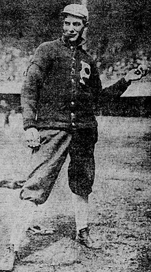 A man in a dark baseball uniform and sweater with light cap and socks