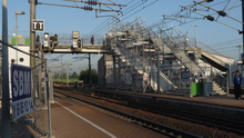 passerelle enjambant les voies avec les escaliers menant au quai central en cours de travaux et une volée d'escaliers provisoires soutenus par des échafaudages, au premier plan 2 voies et caténaires