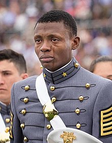 Bust photo of a young black man; he is wearing an old-fashioned military uniform, looking to the camera's left, and crying.