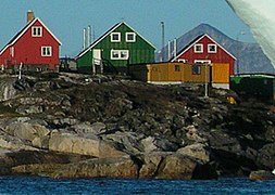 Photographie en couleurs de trois maisons et d'un bâtiment en bois surplombant la mer.