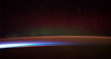 Earth's atmosphere seen from space. From the bottom, afterglow illuminates the troposphere in orange with silhouettes of clouds, and the stratosphere in white and blue. Next the mesosphere (pink) and the pink line of airglow of the lower thermosphere (dark), which hosts green and red aurorae over several hundred kilometers.