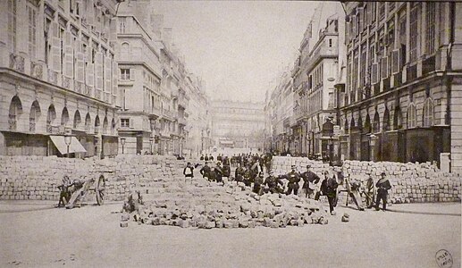 Photographie représentant des hommes en armes devant une barricade érigée place Vendôme à Paris en 1871 lors des évènements de la Commune