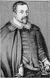 A man with short hair, moustache and goatee beard, wearing a ruff, decorated tunic and a cloak; his left hand holds the handle of a sword