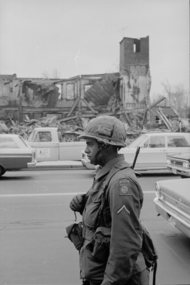 An 82nd paratrooper on guard duty near the passing motorists and the destroyed building on 8 April 1968, during the rioting in Washington, D.C. DC riots Soldier.png