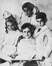 A woman sits behind 3 children holding a book