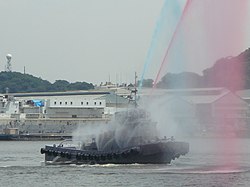 放水銃2丁を用いて歓迎の放水をすると共に、自衛散水装置を作動させる曳船68号（YT-68）。