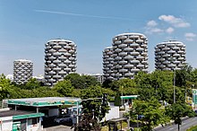 Five of the building towers, with trees in the foreground and a petrol garage