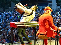 Musician Michael Guerra playing an accordion while facing an audience. To his right is keyboardist Jerry Dale McFadden, playing a piano keyboard while his back is to the camera