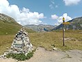 Panneaux de randonnée et borne en pierres sèches au col avec au loin la tête Sud des Fours et le col de la Croix du Bonhomme.