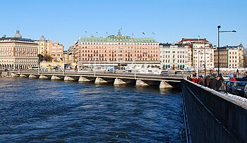 Strömbron under uppförande 1946 och sedd från samma plats år 2010. Bron grundlades provisoriskt på träpålar, som sticker upp över vattenytan, vilket framgår på bilden från 1946. I bakgrunden syns Grand Hôtel innan takvåningen påfördes.