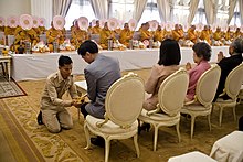 Former Thai prime minister holding a vessel and pouring water during a ceremony with a large number of monks.