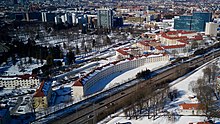 Foto aus der Luft von städtischer Bebauung mit Blockbauten im Vordergrund und Hochhäusern im Hintergrund.