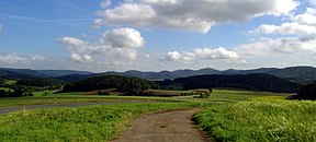 Blick auf die Damshäuser Kuppen mit dem 498 m hohen Rimberg (mittig, teils verdeckt) im äußersten Nordosten des Gladenbacher Berglandes. Der breite, 474 m hohe Wollenberg (links) gehört bereits zum Rothaargebirge