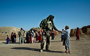 A 7th SFG Special Forces medic gives a young boy a coloring book during a meeting with village religious leaders to gain their support and obtain information, Afghanistan 2008. Special Forces Medic in Afghanistan (wide view).jpg