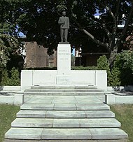 Photographie couleur d'une statue apposée sur une base en pierre blanche.