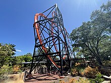 The twisting track of Tigris pictured from the queue line area with landscaping surrounding the roller coaster