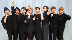 The eight members of Stray Kids, all in black, look forward