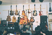 coffeehouse-like concert at place with many guitars on wall