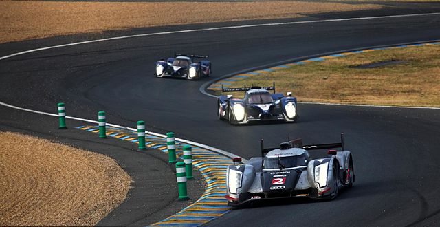 Three sports prototype racing drivers being driven around a corner on a motor racing circuit