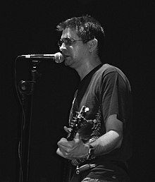 Steve Albini playing guitar, wearing a black t-shirt and ripped blue jeans