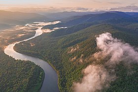 Photographie aérienne d'une rivière à travers un paysage montagneux très vert.