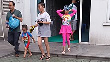 An adult walks with three children. The children are dressed to go swimming.