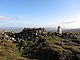 A mound of stones on a grassy summit, next to a concrete trigonometry point