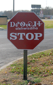 一个红底白边、正八边形的停车标志，上面有三行文字。上面那行写的是切罗基音节文字，下面那行写的是英语，中间还有一行小字，写的是上面那行切罗基音节文字对应的拉丁转写。