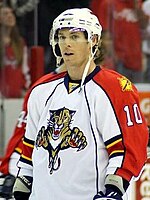 A player stands straight up looking off into the distance. He is wearing a "traditional" Panthers white jersey with a white helmet with a visor.