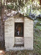 Photographie d'une statue et de son oratoire forestier avec ses parois en pierres restaurées.