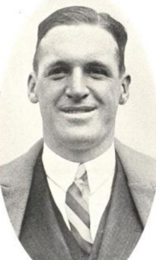 Smiling white man wearing a suit and tie; he is clean-shaven and has short side-parted hair