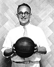A man holding a basketball. He is wearing a white shirt and tie.