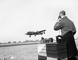 A black and white image of a Royal Air Force Sergeant on the telephone informing Air Traffic Control of a Halifax aircraft arriving at the base