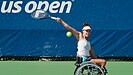 Dana Mathewson sitzt im Rollstuhl und schlägt einen Tennisball, dessen Bewegung im Bild erkannt werden kann. Im Hintergrund sind die Banden mit US Open beschriftet.