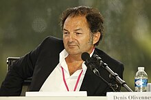 Photo d'Olivennes lors d'une conférence de presse en 2009, les cheveux en bataille, le front dégarni, situé devant deux micros et regardant sur sa droite.