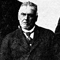 Black and white photo of a white man, with a seemingly angry face, wearing a suit and a tie