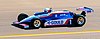 The side view of a blue, red and white racing car with the number 1 in white on its side being driven on a race track