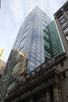 The dark-blue and light-blue patterned glass facade of the building, as seen from 45th Street. The Lyceum Theatre, a short stone building with ornate decoration, is next to 1540 Broadway.